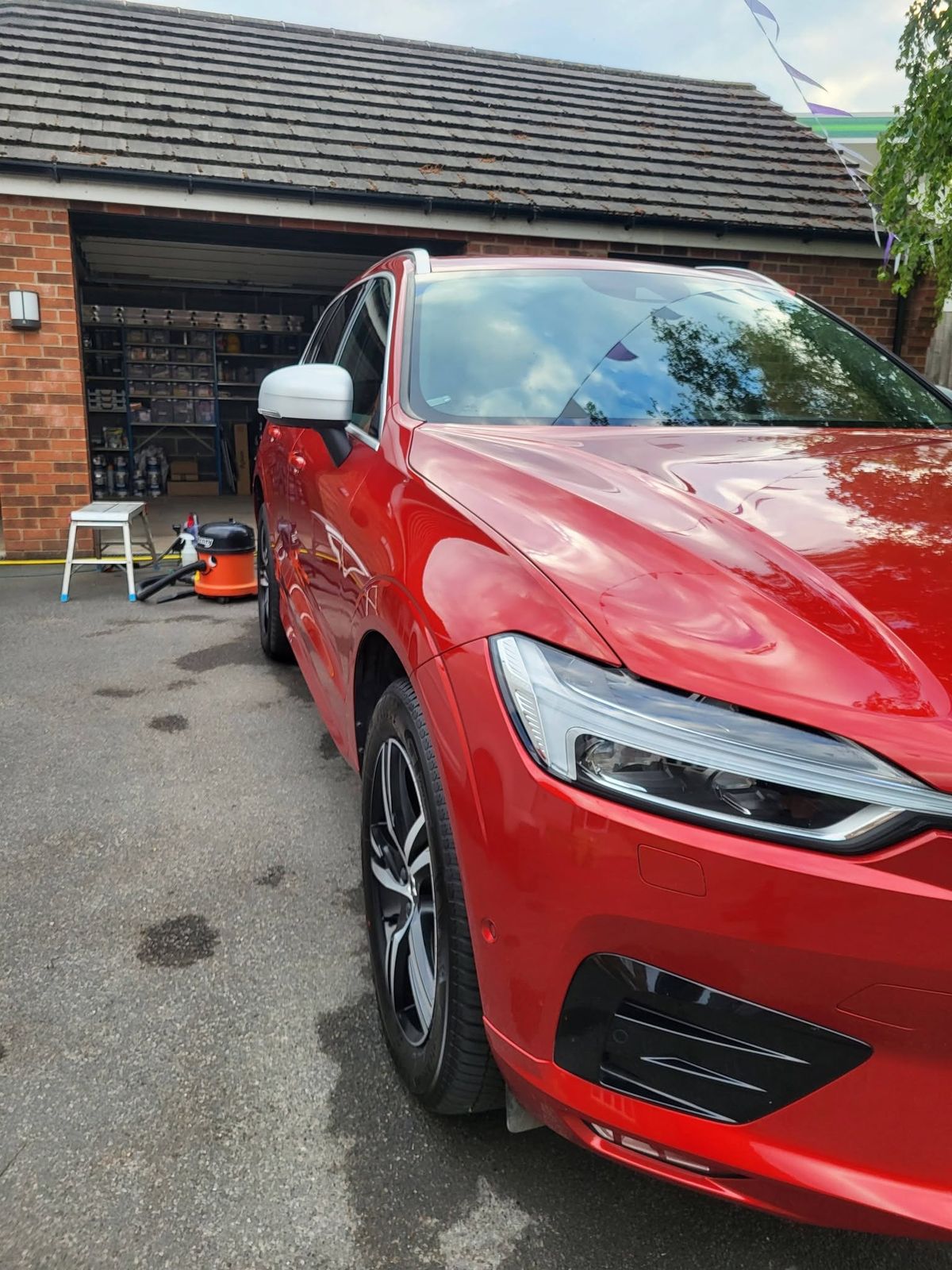Tight crop of a red car's bonnet and wing after valeting, with sky and trees reflected in the paint